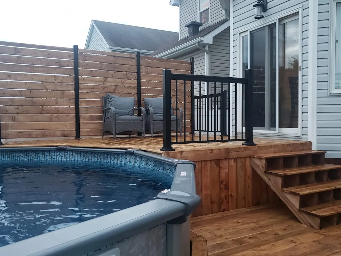 Cedar deck with black railing and steps leading down to an above-ground pool