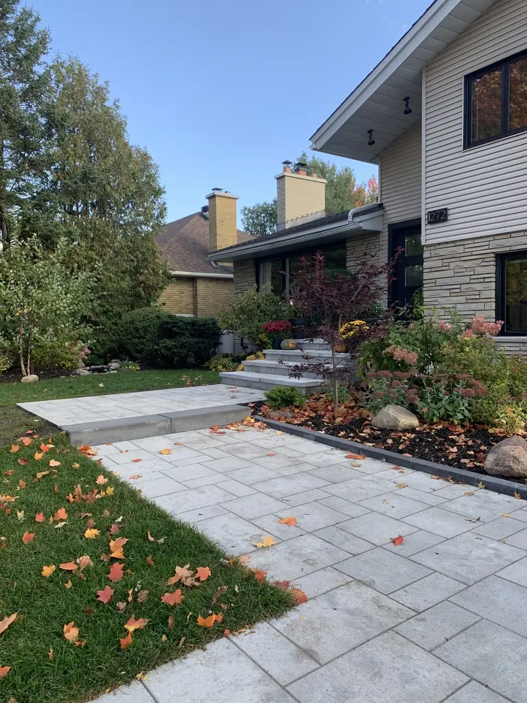 New grey interlock walkway curving past garden beds toward a house