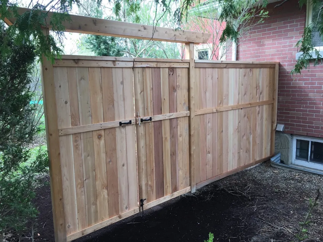 Tall cedar privacy fence and double gate beside a brick house