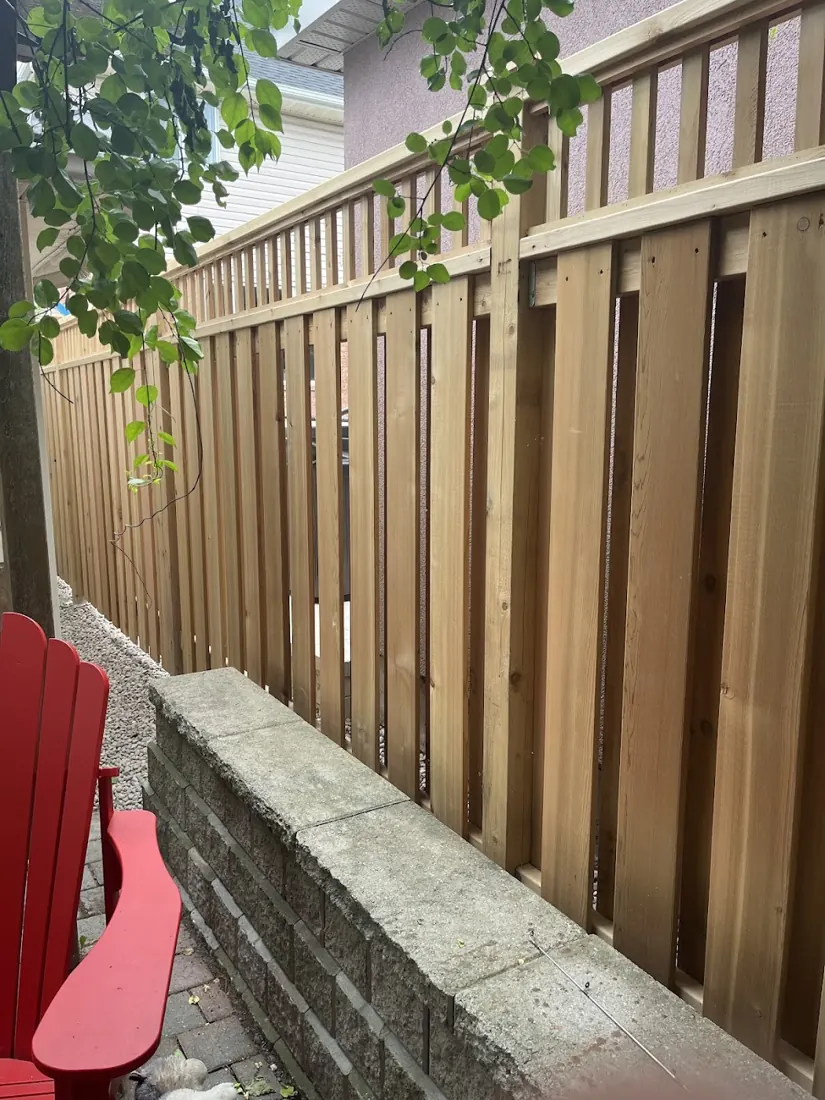 Cedar privacy fence with a red chair beside a stone retaining wall